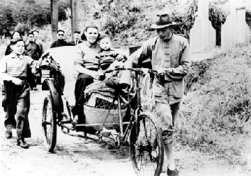 坐三輪車-民國38年（1949年），在奉化老家，蔣方良女士抱著二兒子孝武坐三輪車。大兒子孝文追隨其後。帶著墨鏡的經國先生在遠處望著他們微笑。